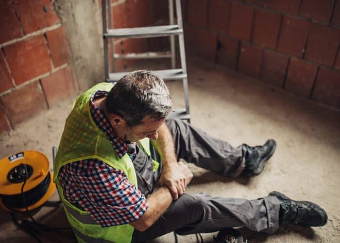 A male construction sitting on the ground holding his injured wrist