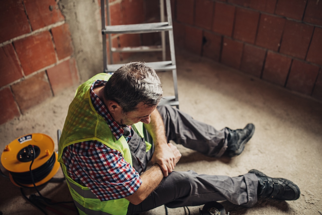 A male construction sitting on the ground holding his injured wrist
