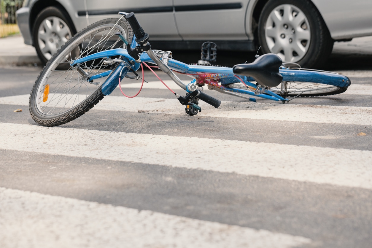 A bicycle laying on the ground in a crosswalk with a car next to it