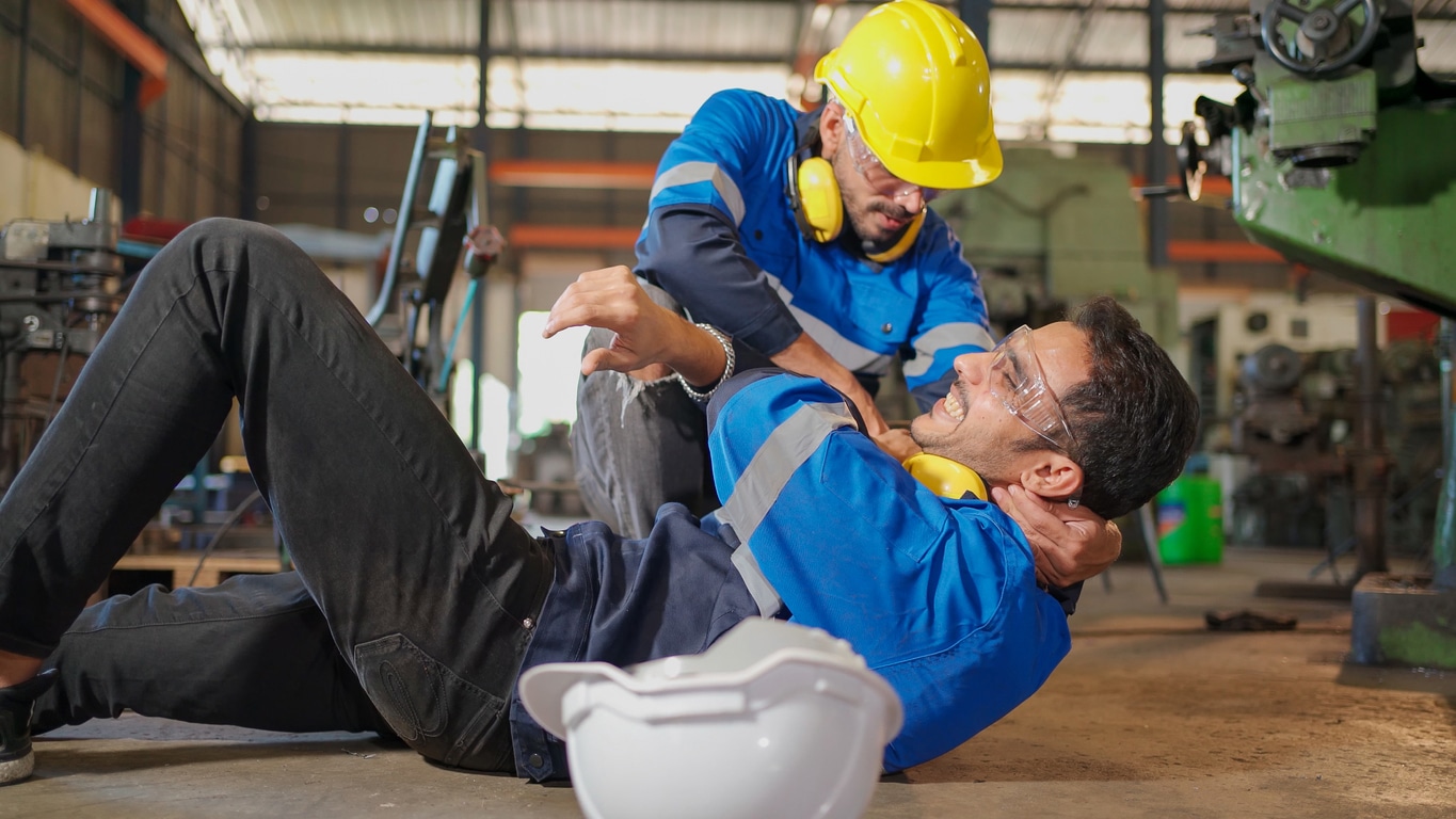 Injured construction worker laying on the ground in pain being held up by his coworker