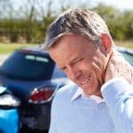 An older man who standing in front of a rear end car accident holding his neck in pain
