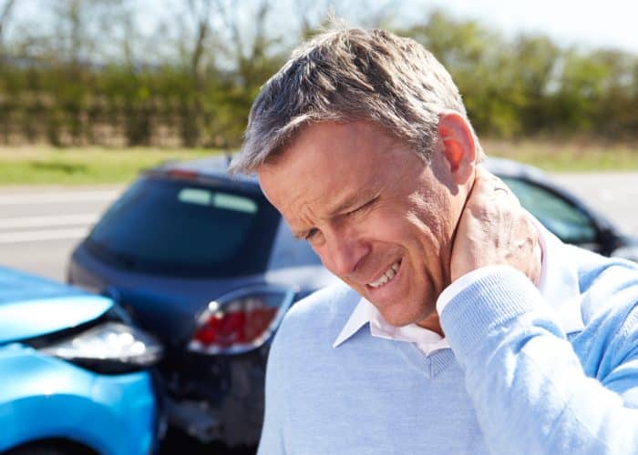 An older man who standing in front of a rear end car accident holding his neck in pain