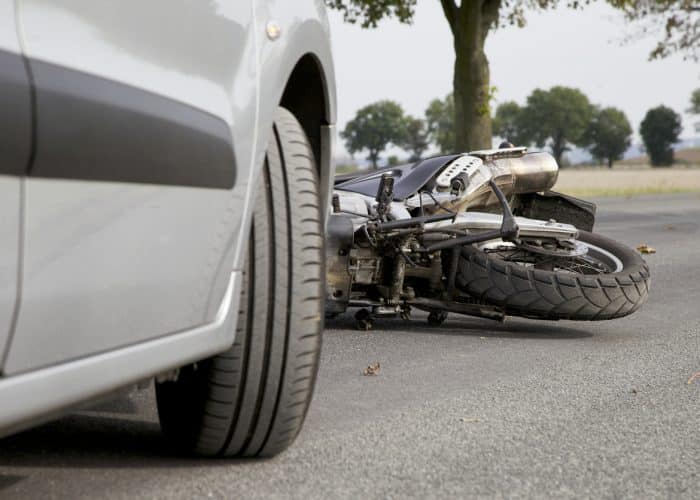 Motorcycle laying on the street behind a car after an accident