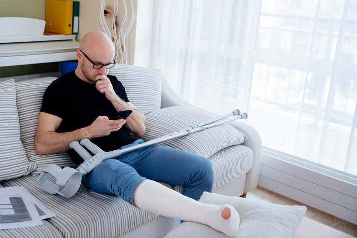 A man with glasses with a broken leg is sitting on the couch at home. Calls the insurer for compensation - the role of a workers' compensation lawyer
