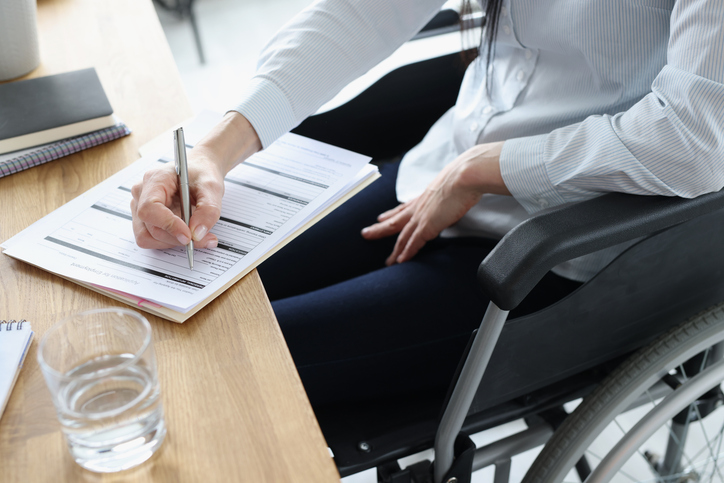 Person in wheelchair signing a document- Can you claim disability and work part-time?